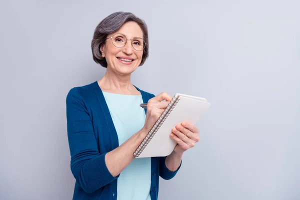 Portrait photo d'une femme d'affaires âgée portant des lunettes écrivant des notes avec un stylo lors d'une entrevue isolée sur fond gris — Photo