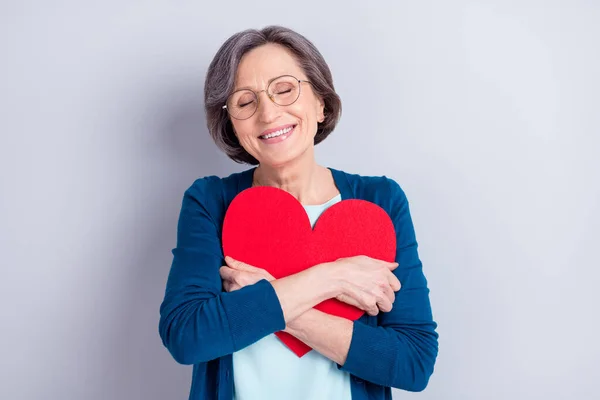 Foto de sonho feliz afetuoso mulher velha abraço grande forma ouvida papel vermelho isolado no fundo de cor cinza — Fotografia de Stock