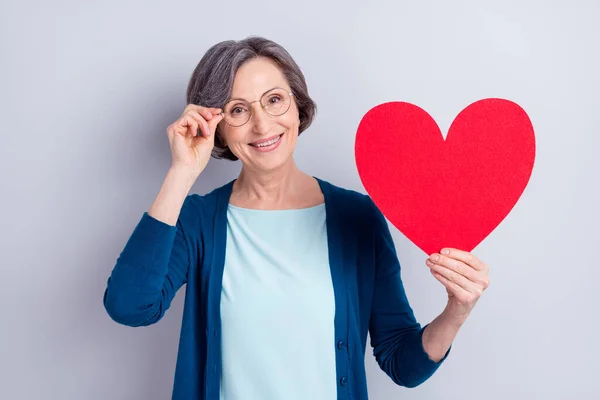 Фотографія весела бабуся показує символ любові червоне серце посміхається в окулярах ізольовано на сірому кольоровому фоні — стокове фото