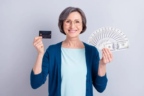Foto di allegra bella vecchia tenere per mano denaro contante carta di credito pagamento isolato su sfondo di colore grigio — Foto Stock