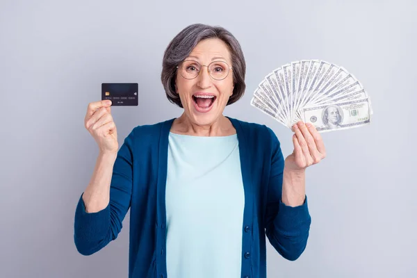 Foto ritratto di donna d'affari stupita che mostra le banconote del dollaro della carta di credito isolate su sfondo di colore grigio — Foto Stock