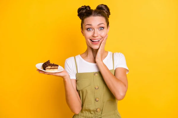 Portrait of impressed brunette nice lady hold piece of cake wear bright t-shirt overall isolated on vivid yellow color background — Stock Photo, Image