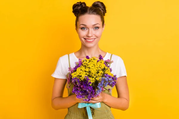 Фото очаровательной юной леди держать букет полевых цветов сияющие улыбки носить зеленый общий изолированный желтый фон — стоковое фото