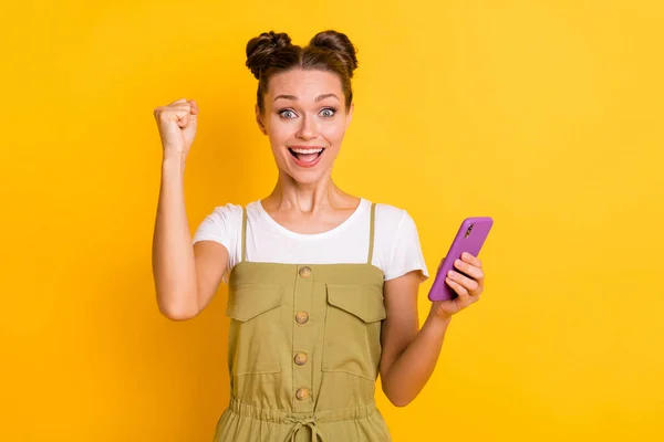 Foto de excitado louco senhora levantar punho segurar telefone boca aberta desgaste verde geral isolado fundo amarelo — Fotografia de Stock