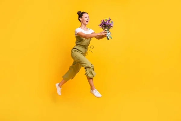 Full length μέγεθος σώματος άποψη του όμορφου trendy χαρούμενο κορίτσι άλμα πηγαίνει μεταφέρουν φρέσκα λουλούδια απομονώνονται σε φωτεινό κίτρινο χρώμα φόντο — Φωτογραφία Αρχείου