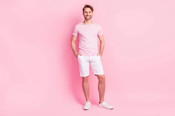 Photo of pretty funny young gentleman dressed casual t-shirt arms shorts pockets smiling isolated pink color background — Stock Photo, Image