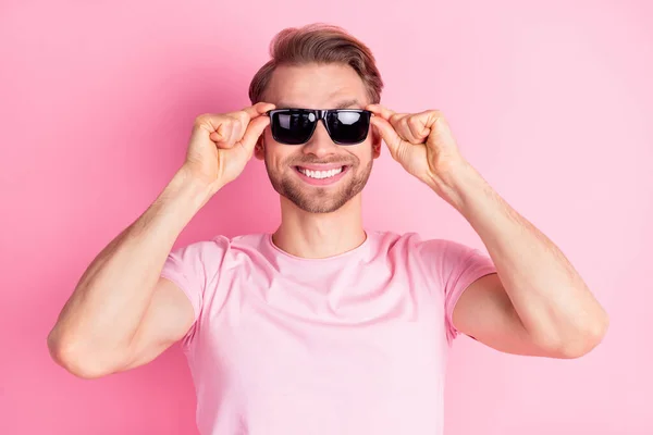 Foto di grazioso affascinante giovane gentiluomo vestito casual t-shirt braccia occhiali scuri sorridente isolato colore rosa sfondo — Foto Stock