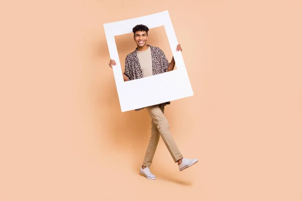 Retrato de longitud completa de alegre piel oscura chico manos mantenga marco de papel radiante sonrisa aislada sobre fondo de color beige —  Fotos de Stock