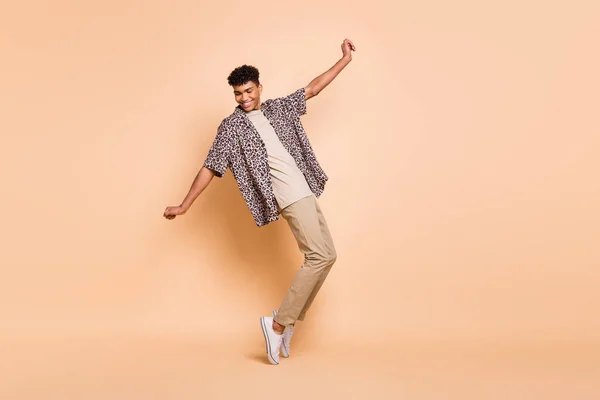 Foto de perfil em tamanho real do cara otimista morena dança desgaste moderno camisa calças tênis isolado no fundo cor bege — Fotografia de Stock