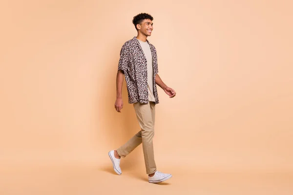 フルサイズプロフィール写真のブルネット楽観的な男行く身に着けている現代的なシャツパンツスニーカー絶縁上ベージュ色背景 — ストック写真
