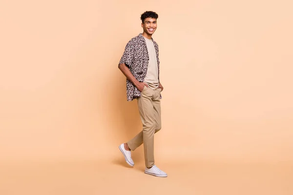 Full body profiel foto van vrolijke donkere huid persoon lopen look camera geïsoleerd op beige kleur achtergrond — Stockfoto