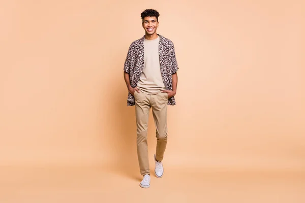 Full size foto van brunet optimistische man gaan dragen moderne shirt broek sneakers geïsoleerd op beige kleur achtergrond — Stockfoto