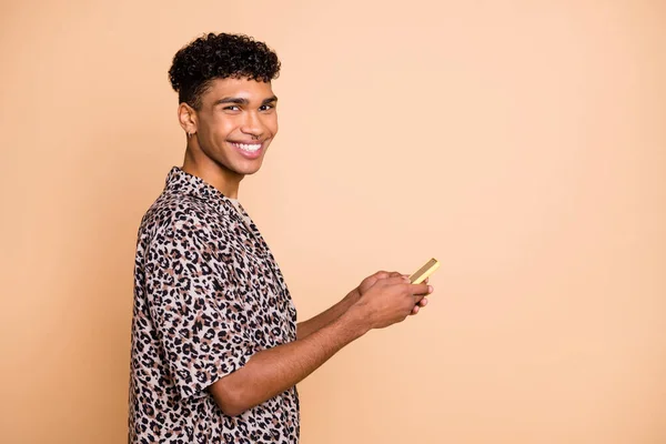 Profiel portret van knappe positieve donkere huid man tand glimlach kijken camera geïsoleerd op beige kleur achtergrond — Stockfoto