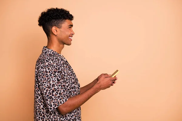 Profiel portret van brunet optimistische man houden telefoon look lege ruimte dragen modern shirt geïsoleerd op beige kleur achtergrond — Stockfoto