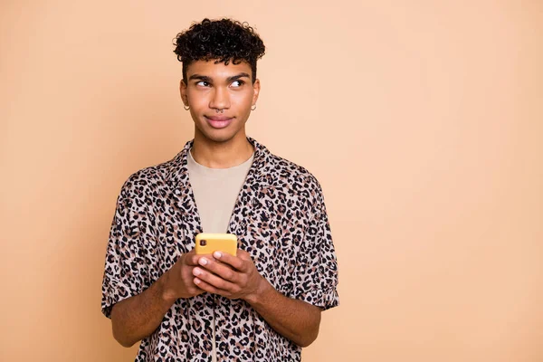 Portret van brunet optimistische man houden telefoon look lege ruimte dragen modern shirt geïsoleerd op pastel beige kleur achtergrond — Stockfoto