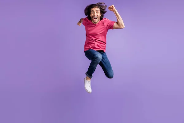 Foto de tamaño completo de optimista chico morena agradable salto usar pantalones vaqueros camiseta rosa aislados sobre fondo violeta —  Fotos de Stock