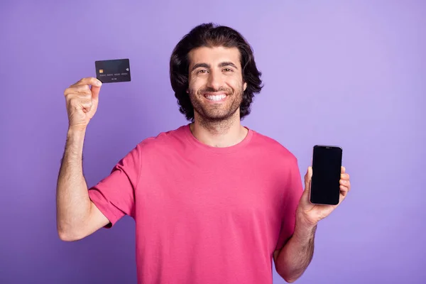 Foto van optimistisch mooie brunet guy hold card telefoon dragen roze t-shirt geïsoleerd op pastel violet kleur achtergrond — Stockfoto