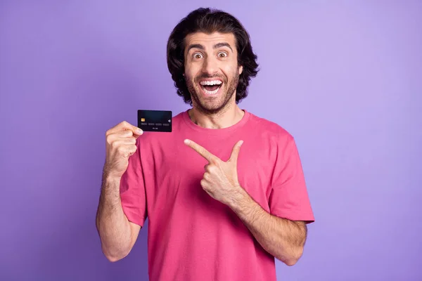 Foto de impressionado funky jovem desgaste rosa t-shirt apontando dedo cartão de banco isolado cor violeta fundo — Fotografia de Stock