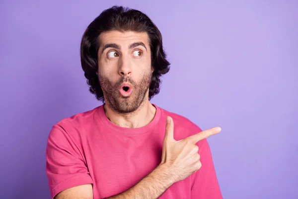 Photo of impressed funky young man wear pink t-shirt looking pointing empty space isolated violet color background — Stock Photo, Image