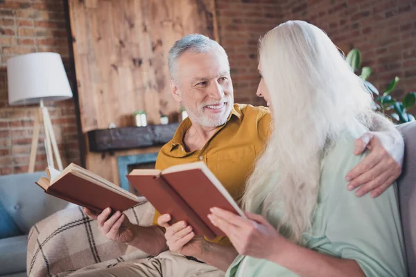 Retrato de agradable anciano cuidado alegre pareja abrazo sentado en sofá lectura libro estancia en casa ladrillo loft interior casa interior — Foto de Stock