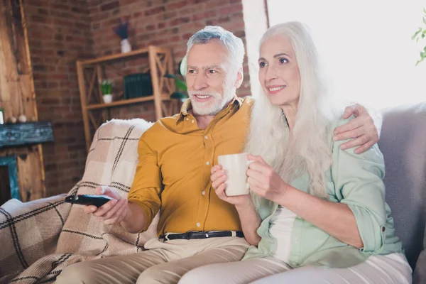 Fénykép az öreg ősz hajú nyugdíjas pár ül kanapén teát nézni TV beltéri házban otthon — Stock Fotó