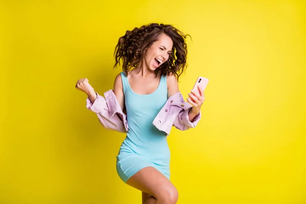 Foto von glücklich aufgeregt verrückt lächelnd Mädchen heben die Fäuste in Sieg Erfolg gewinnen Lotterie in Telefon isoliert auf gelbem Hintergrund — Stockfoto