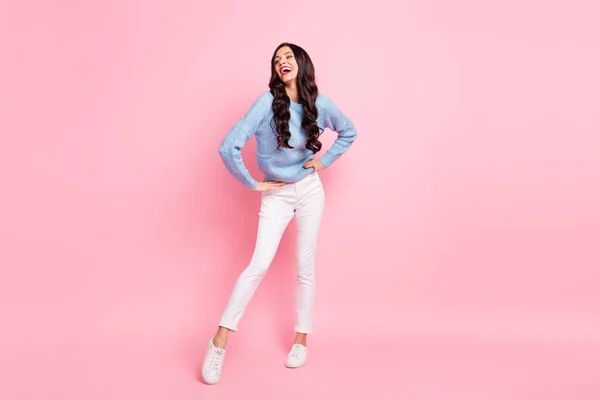 Foto av glada sorglösa flicka händer höfter ser tomt utrymme bära blå pullover byxor skor isolerad rosa färg bakgrund — Stockfoto