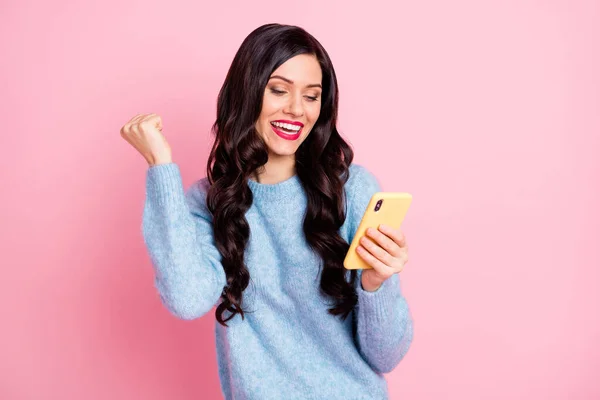 Foto von jungen Mädchen halten Telefon heben Faust Blick Bildschirm tragen blauen Pullover isoliert rosa Farbe Hintergrund — Stockfoto