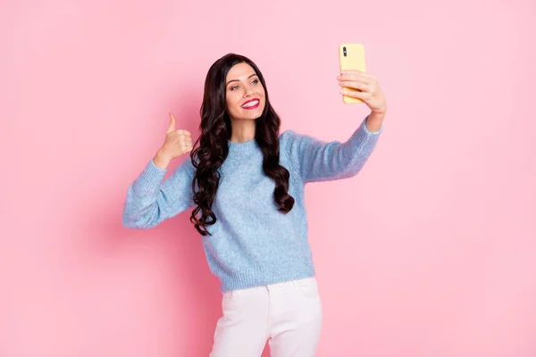Фото милої леді тримає телефон, знімаючи селфі, піднімаючи великий палець вгору, одяг синій пуловер ізольований рожевий колір фону — стокове фото
