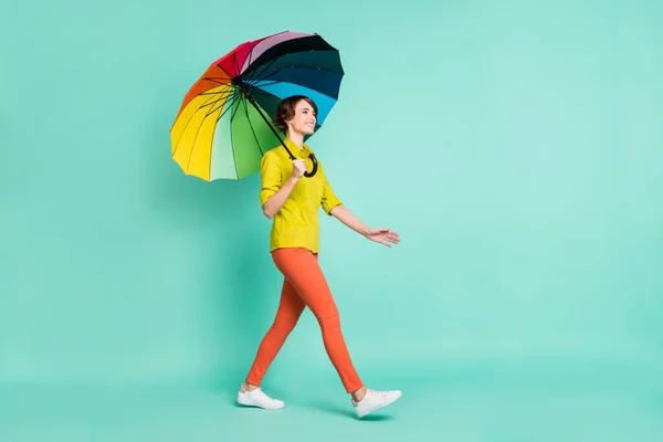 Вид в полный рост на привлекательную жизнерадостную девушку с зонтиком в руках, одинокую на ярко-синем цветовом фоне — стоковое фото