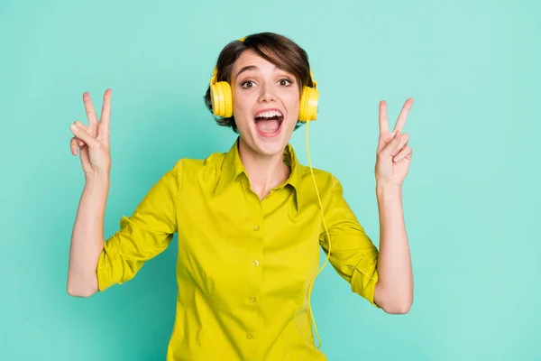 Zdjęcie portret funky dziewczyna słuchanie muzyki słuchawki pokazujące v-sign izolowane na żywe turkusowe tło — Zdjęcie stockowe