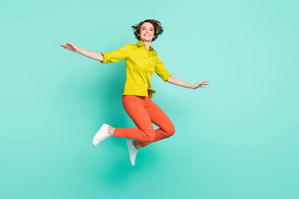 Longitud completa tamaño del cuerpo foto de salto de mujer alta con pantalones de color naranja camisa verde aislado vibrante color turquesa fondo — Foto de Stock