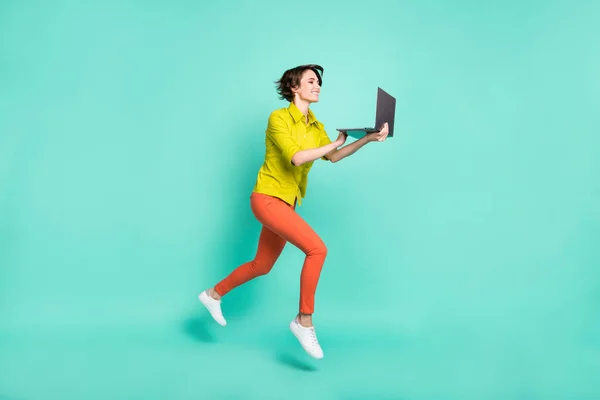 Tamanho do corpo de comprimento total vista de menina alegre atraente pulando usando laptop isolado no fundo de cor azul brilhante — Fotografia de Stock