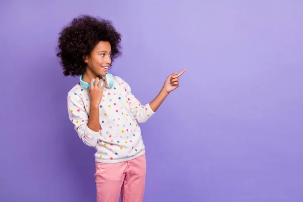 Foto de morena afro americana niña punto espacio vacío usar auriculares pantalones rosados jersey blanco aislado sobre fondo de color violeta —  Fotos de Stock