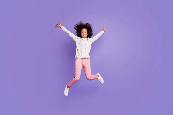 Foto em tamanho completo de feliz afro americano menina salto desgaste rosa calças branco jumper isolado no fundo cor roxa — Fotografia de Stock