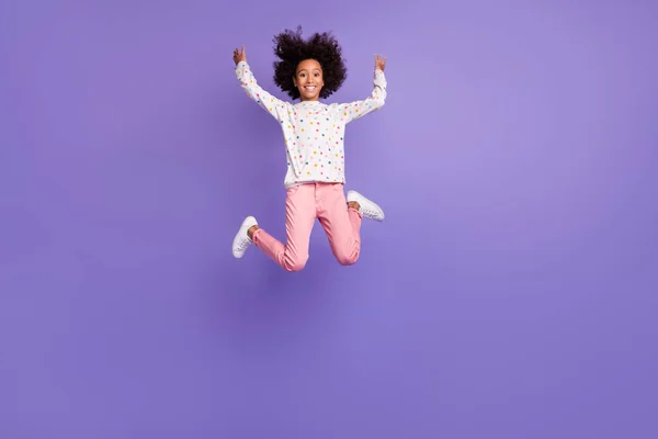 Full size van brunette afro amerikaans klein mooi meisje springen dragen roze broek wit trui geïsoleerd op paars kleur achtergrond — Stockfoto