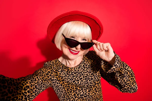 Foto wanita tua yang ceria mengenakan kacamata dingin membuat kamera selfie terisolasi di latar belakang warna merah — Stok Foto