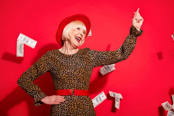 Foto von gealterten Frau glücklich positives Lächeln Blick Zeigefinger leer Raum fliegen Luft Dollars isoliert über rotem Hintergrund — Stockfoto