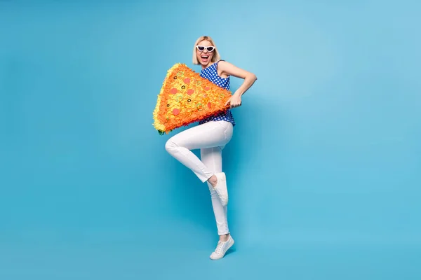 Full längd foto av ung flicka glad positiv leende hålla papper pinata pizza skiva isolerad över blå färg bakgrund — Stockfoto