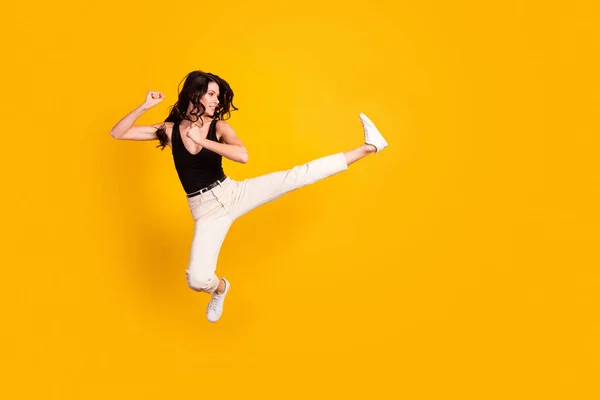 Повна довжина профілю тіла фотографія жінки, що стрибає, б'ючи ногу, як боєць карате, ізольований яскраво-жовтий кольоровий фон — стокове фото