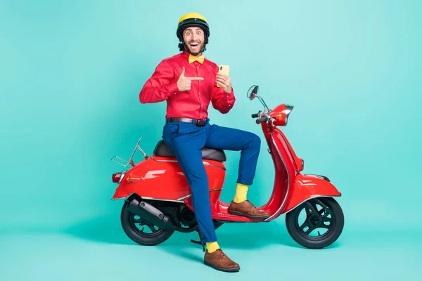 Foto lengkap pria yang gembira dengan helm merekomendasikan ponsel duduk terisolasi di latar belakang warna pirus — Stok Foto