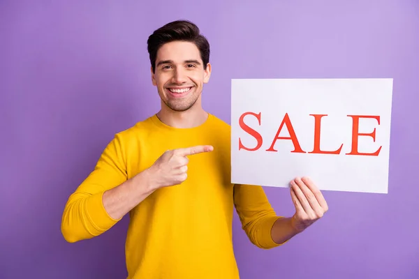 Photo of young man happy positive smile indicate finger paper banner advert sale isolated over violet color background — Stock Photo, Image