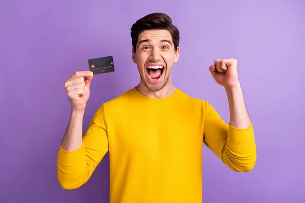 Portret van verbaasd man vuist omhoog vieren open mond schreeuwen ja houden debetkaart geïsoleerd op paarse kleur achtergrond — Stockfoto