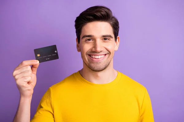 Portret van tevreden jonge man tand glimlach arm houden bankkaart geïsoleerd op paarse kleur achtergrond — Stockfoto