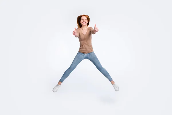 Foto de comprimento total de funky bonito gengibre senhora desgaste bege camisa sorrindo salto mostrando polegares para cima isolado cor branca fundo — Fotografia de Stock