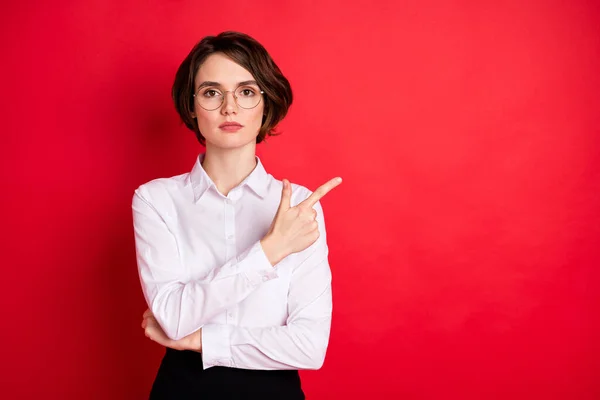 Photo of serious beautiful businesswoman in glasses point finger copysapce advertisement isolated on red color background — Stockfoto