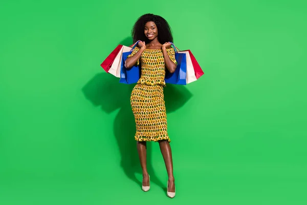 Full body photo of pretty dark skin person arms hold raise bags beaming smile isolated on green color background