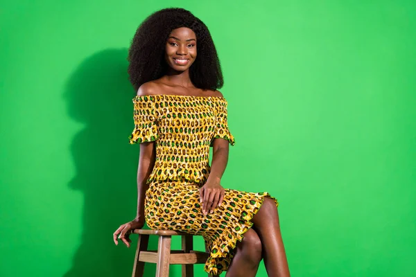 Fénykép a vonzó fekete nő boldog pozitív mosoly ül szék viselni csillogás ruhát elszigetelt zöld színű háttér — Stock Fotó