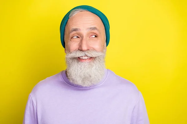 Foto von coolen kniffligen reifen Mann gekleidet lila Pullover Kopfbedeckung lächelnd suchen leeren Raum isoliert gelbe Farbe Hintergrund — Stockfoto