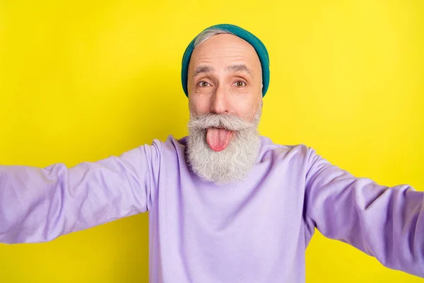 Photo portrait of elder man showing tongue taking selfie smiling isolated on bright yellow color background — Stock Photo, Image